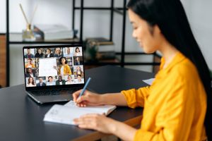 Online education. Smart japanese student girl gains knowledge watching lesson online. Young woman takes notes during webinar, listening lecture on video call. Female teacher and students on a screen monthly webinars